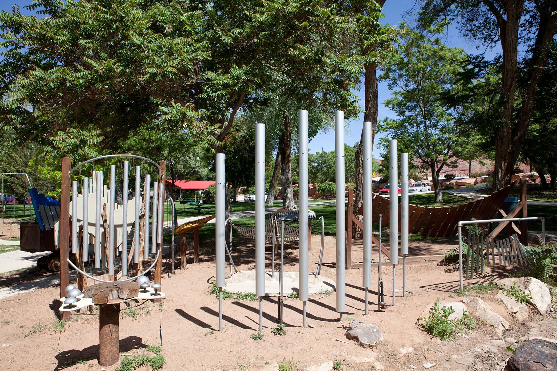 Outdoor musical playground with silver chimes, a wood post and dirt ground.