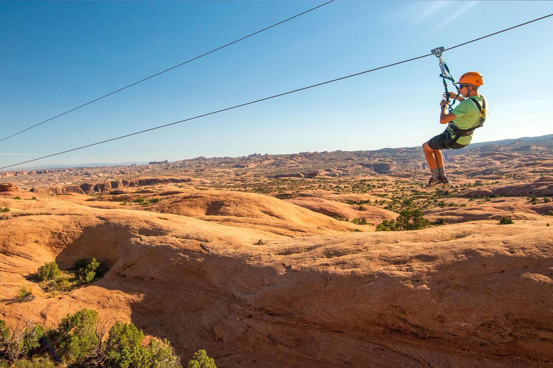 Person ziplining across a desert landscape under a blue sky.