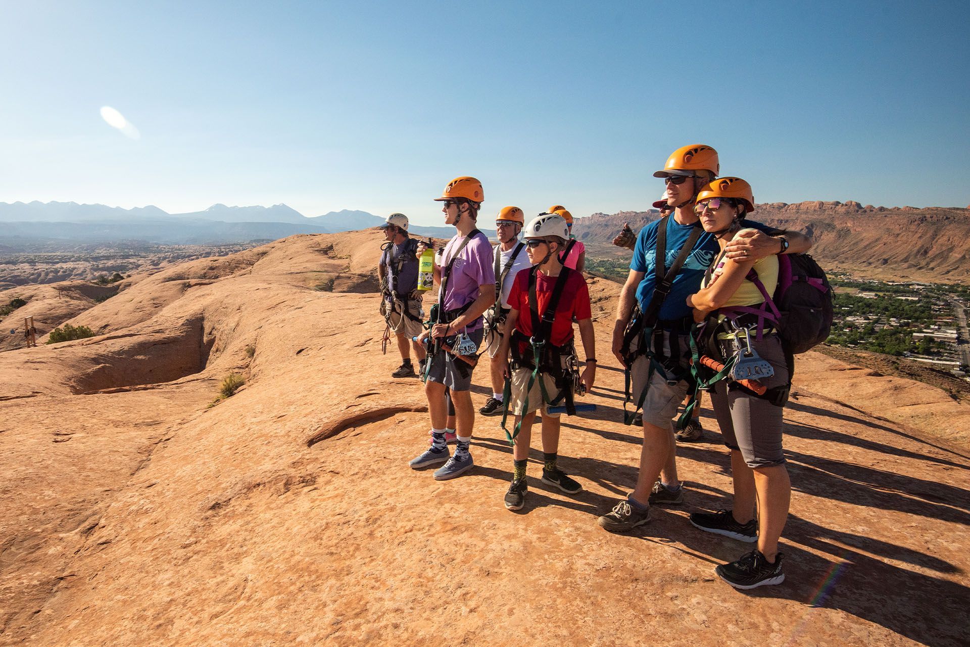 Group of people in helmets and harnesses look out over a canyon vista.