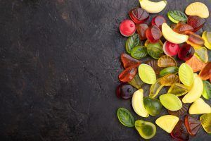 Gummy candies shaped like fruit, in various colors, scattered on a dark textured surface.