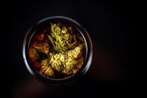 Jar filled with green and brown cannabis buds on a black background.
