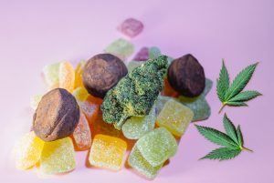 Cannabis bud and edibles on a pink background: gummies, truffles, and two marijuana leaves.