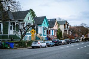 Row of colorful houses with cars parked on the street on a cloudy day.