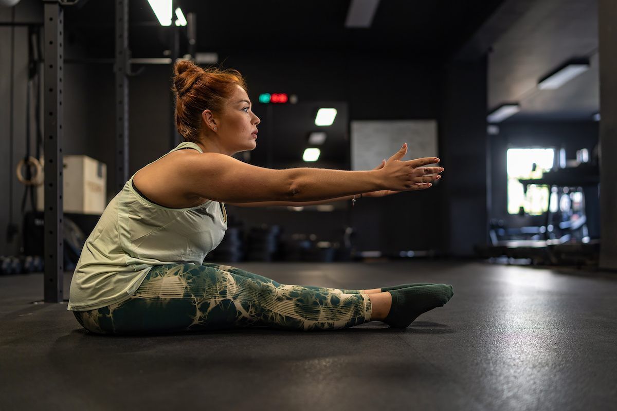 Woman in workout clothes stretching forward in a gym.