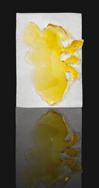 Yellow abstract paint-like shape on a white card, reflected on a dark glossy surface.