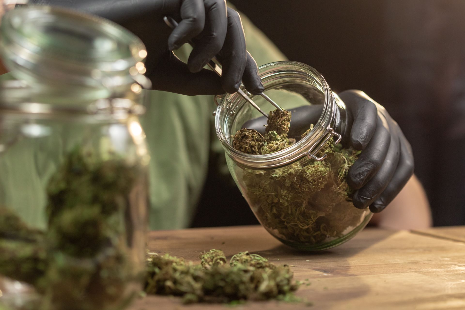 Person wearing black gloves placing cannabis buds into a glass jar.