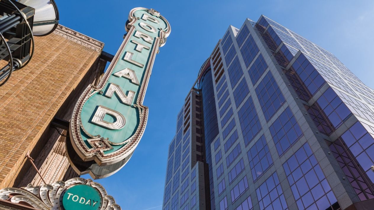 Sign for the historic Ryman Auditorium with a tall modern building in the background against a blue sky.