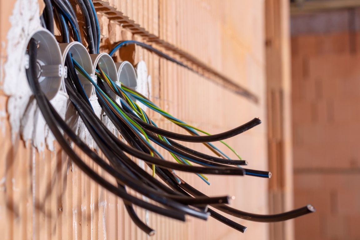 Bundles of black, blue, and green-yellow electrical wires protruding from four wall-mounted junction boxes in a brick wall.