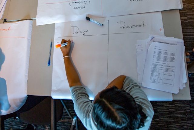 Girl sitting at table with papers and pens working on group development task
