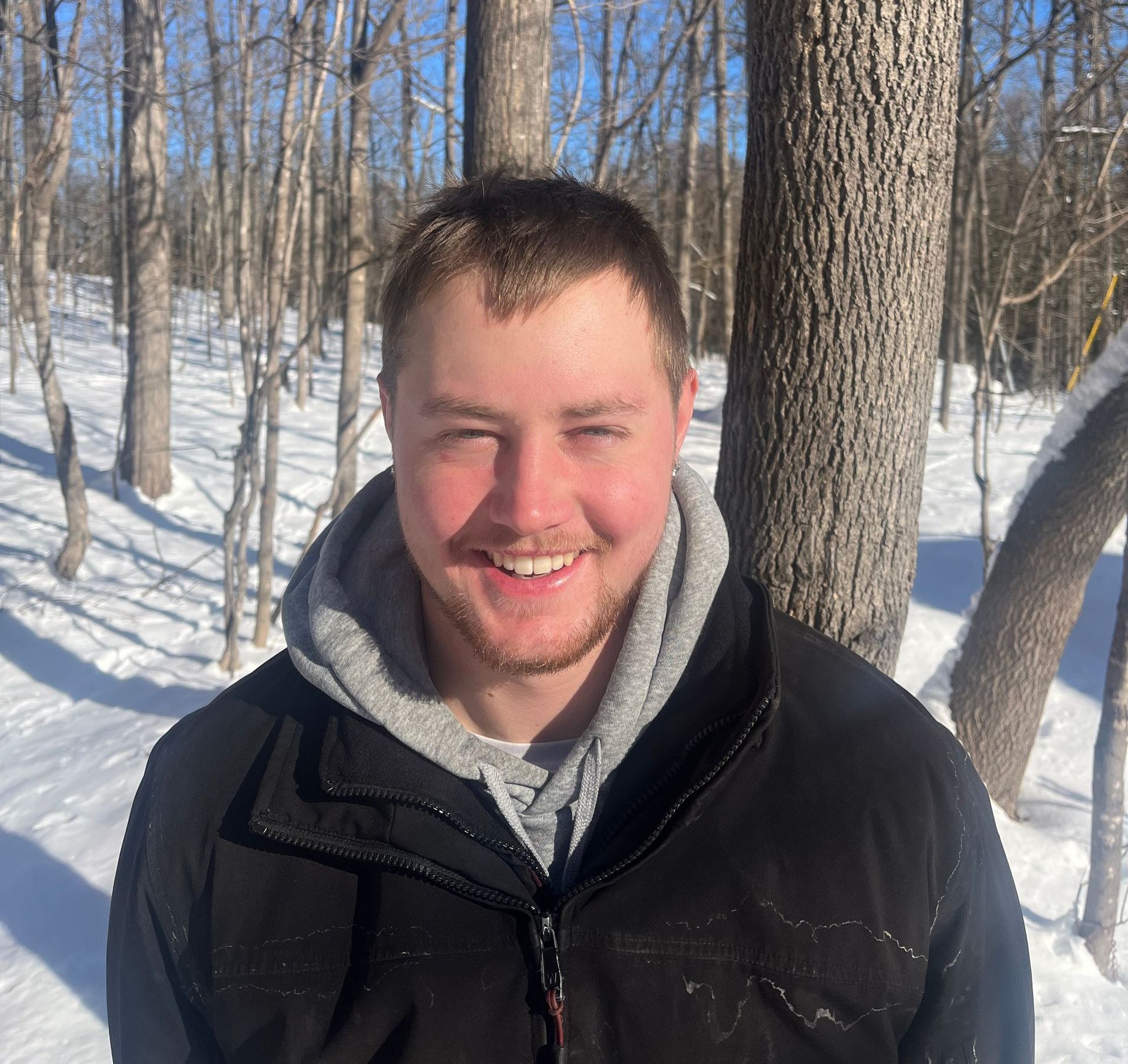 A man in a black jacket is smiling in the snow