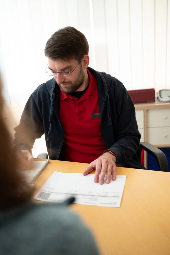 Ein Mann sitzt an einem Tisch und schaut auf ein Blatt Papier.