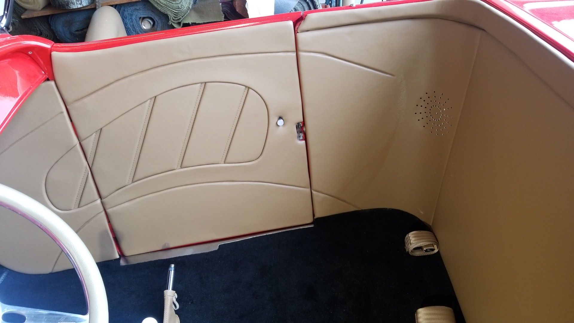Beige car interior panel with stitched leather detailing and a small speaker grille.