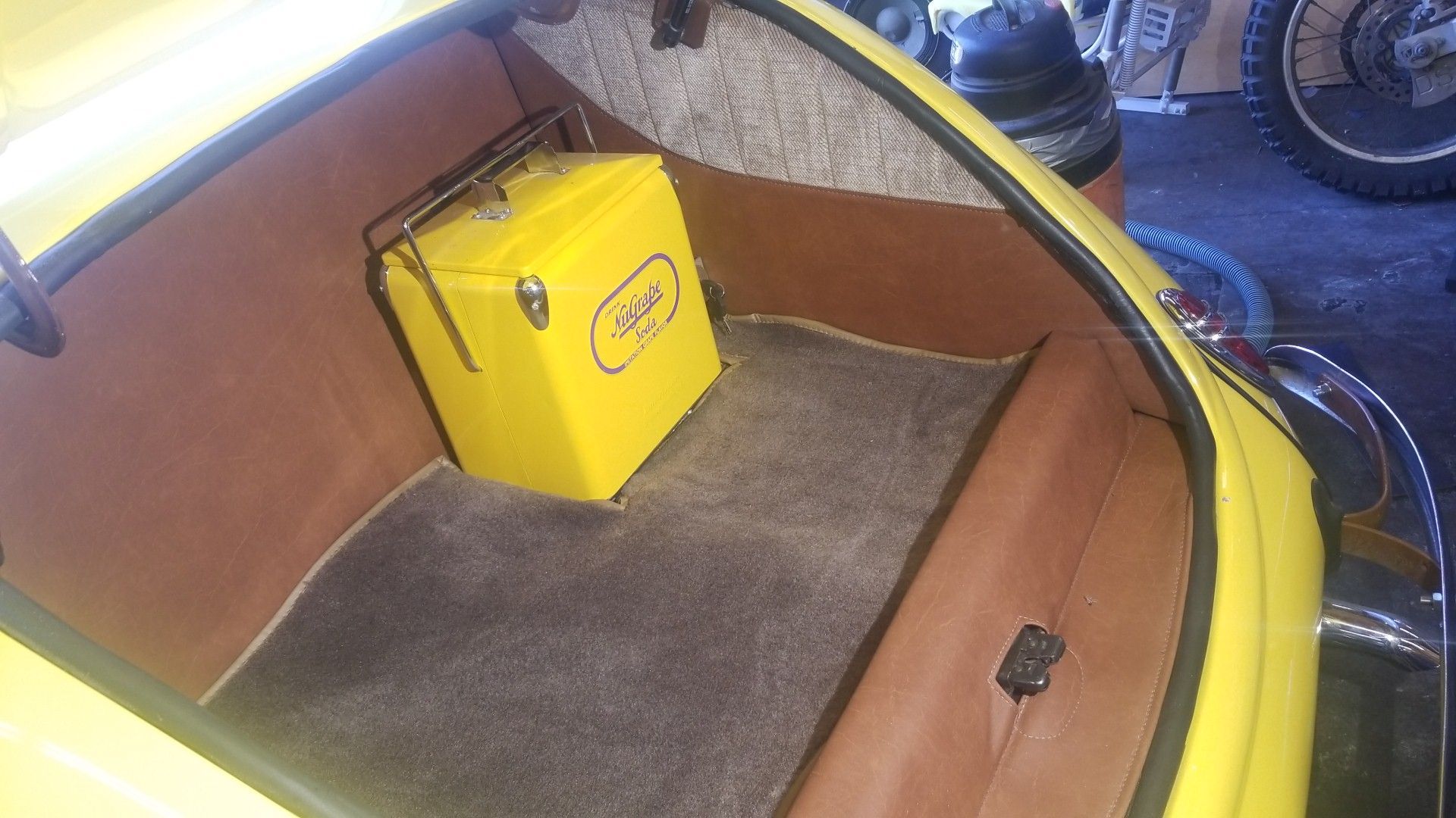 Yellow storage box in the back of a small yellow vehicle interior with brown trim.