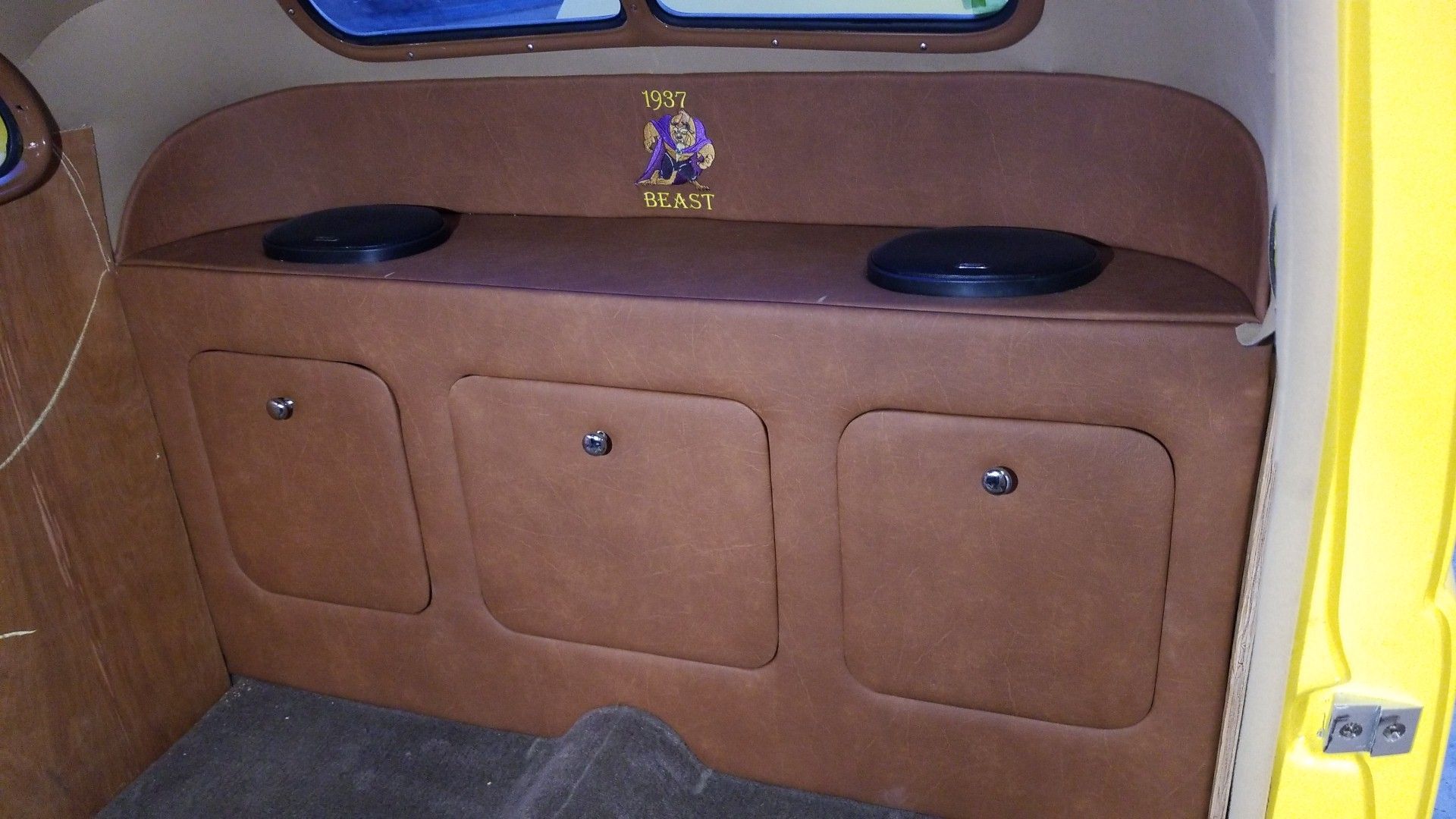 Brown built-in cabinet under a vehicle window with three doors and two black cushions on top.