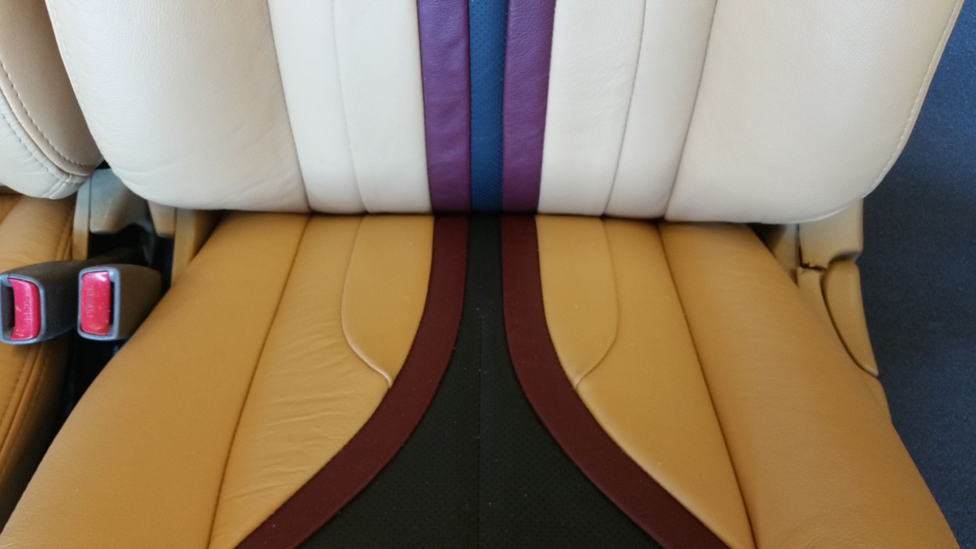 Car seat with tan and white cushions, purple center stripe, and visible pink seat belt buckle