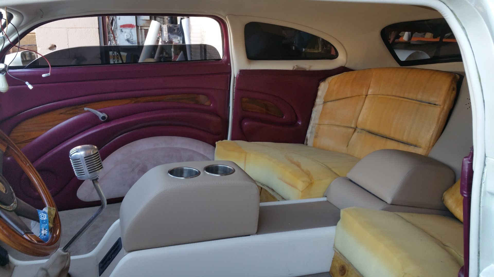 Vintage car interior with maroon and tan upholstery, front and rear seats, and a manual gear shift.