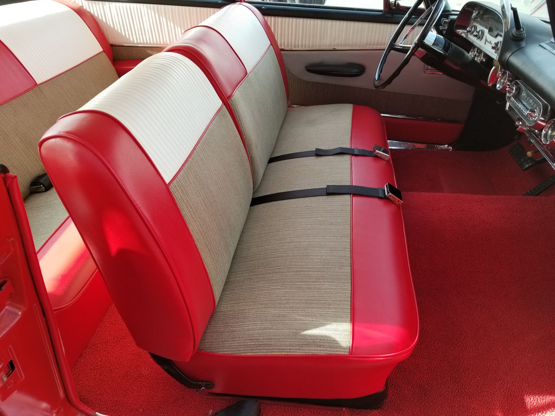 Red-and-white upholstered bench seat inside a vintage car with red carpet and dashboard visible