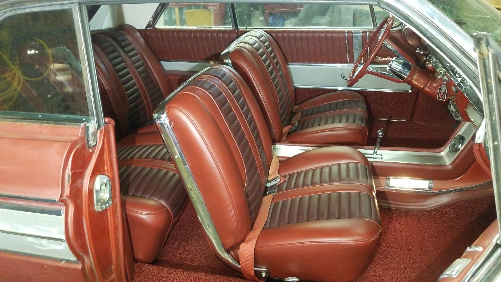 Red leather car interior with striped bucket seats and polished dashboard visible through the open door