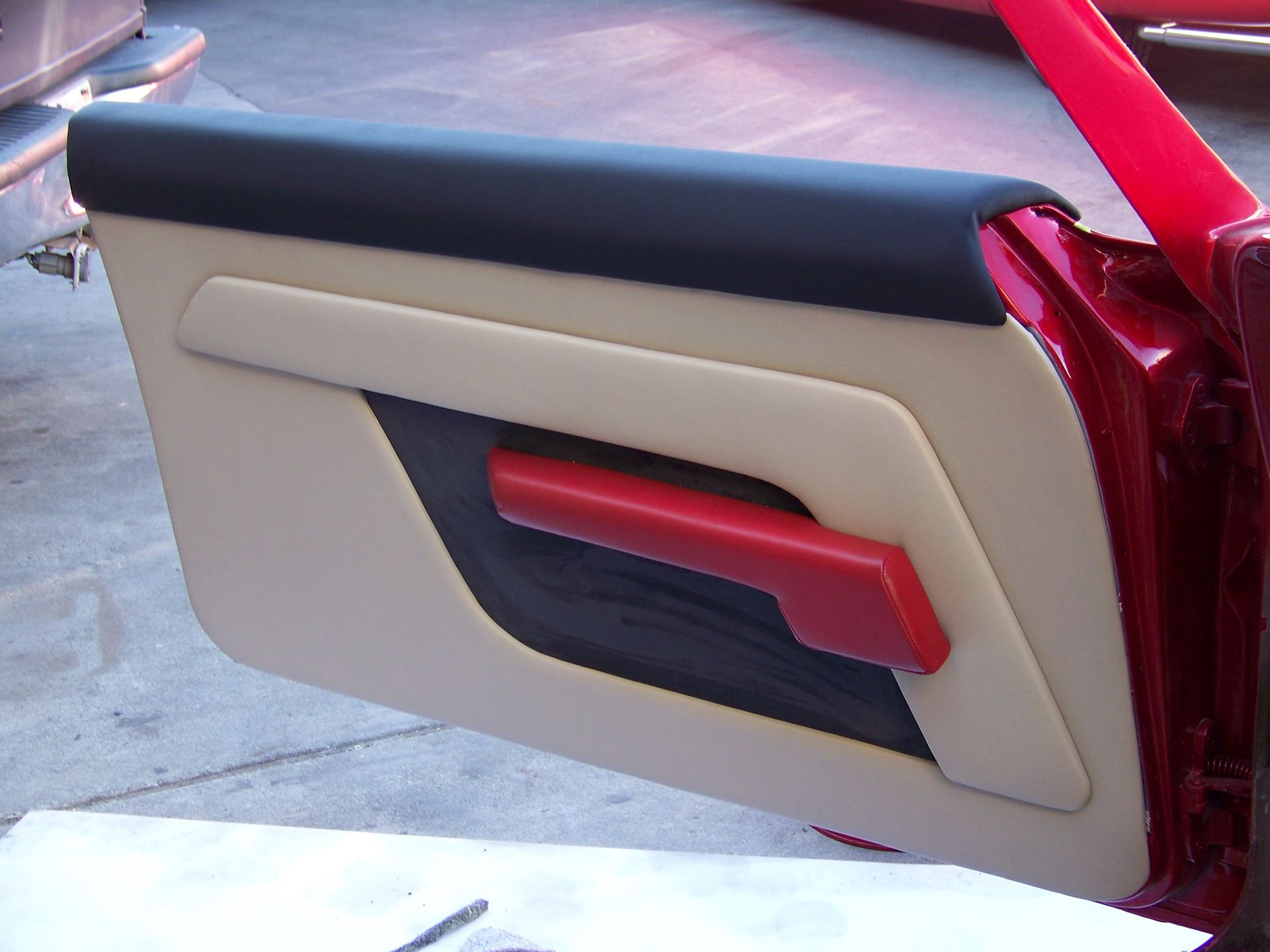 Classic car door panel in beige, black, and red leather upholstery with a red handle.