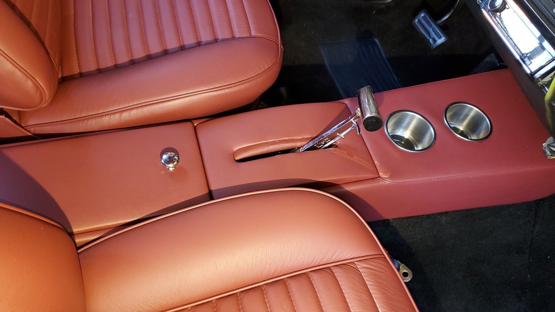 Car interior with brown leather seats and a red center console holding a gear shift and cup holders