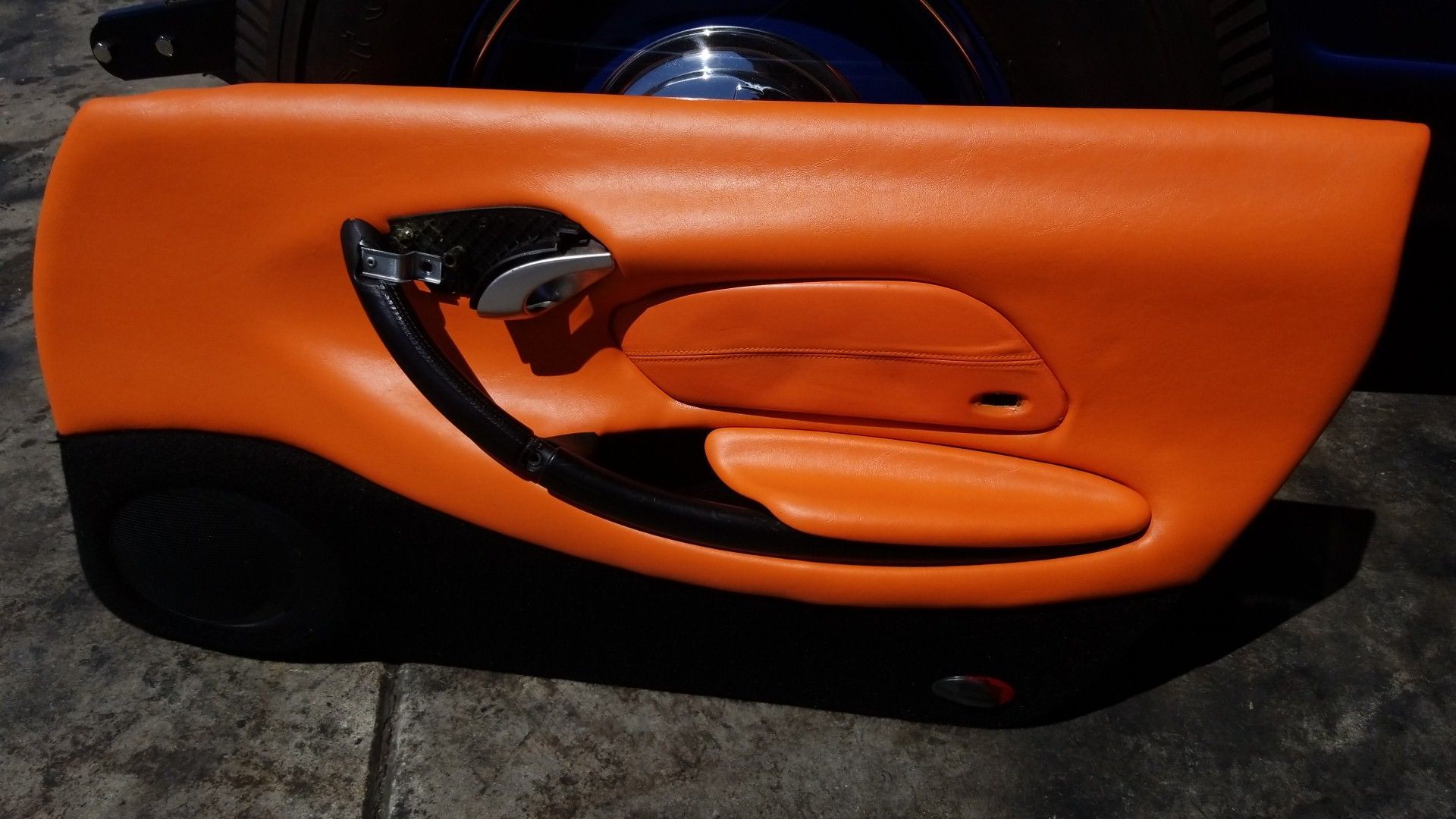 Orange car door panel with black trim and chrome handle lying on a dark floor
