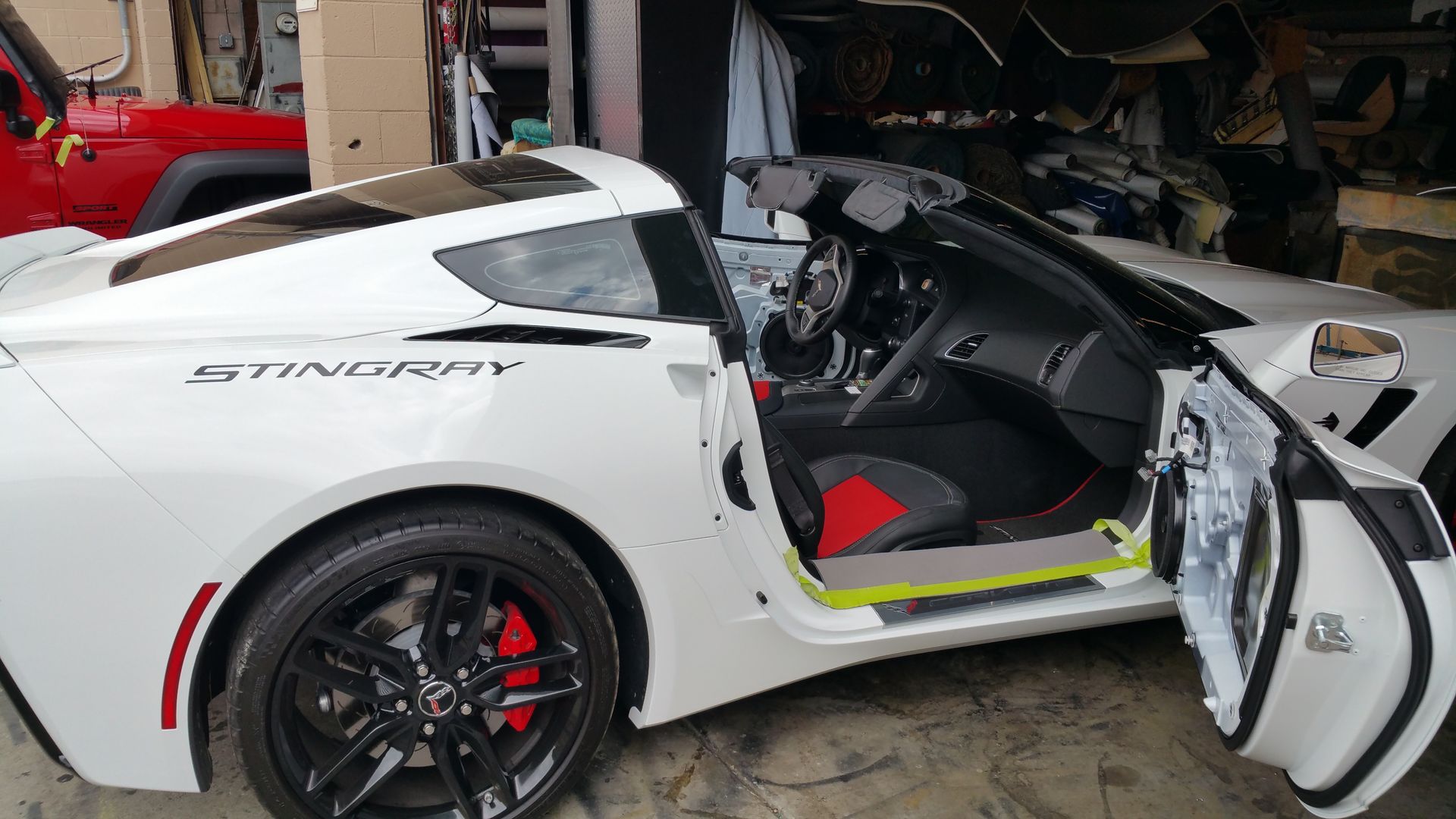 White sports car with gullwing door open in a garage, showing red interior and black wheels