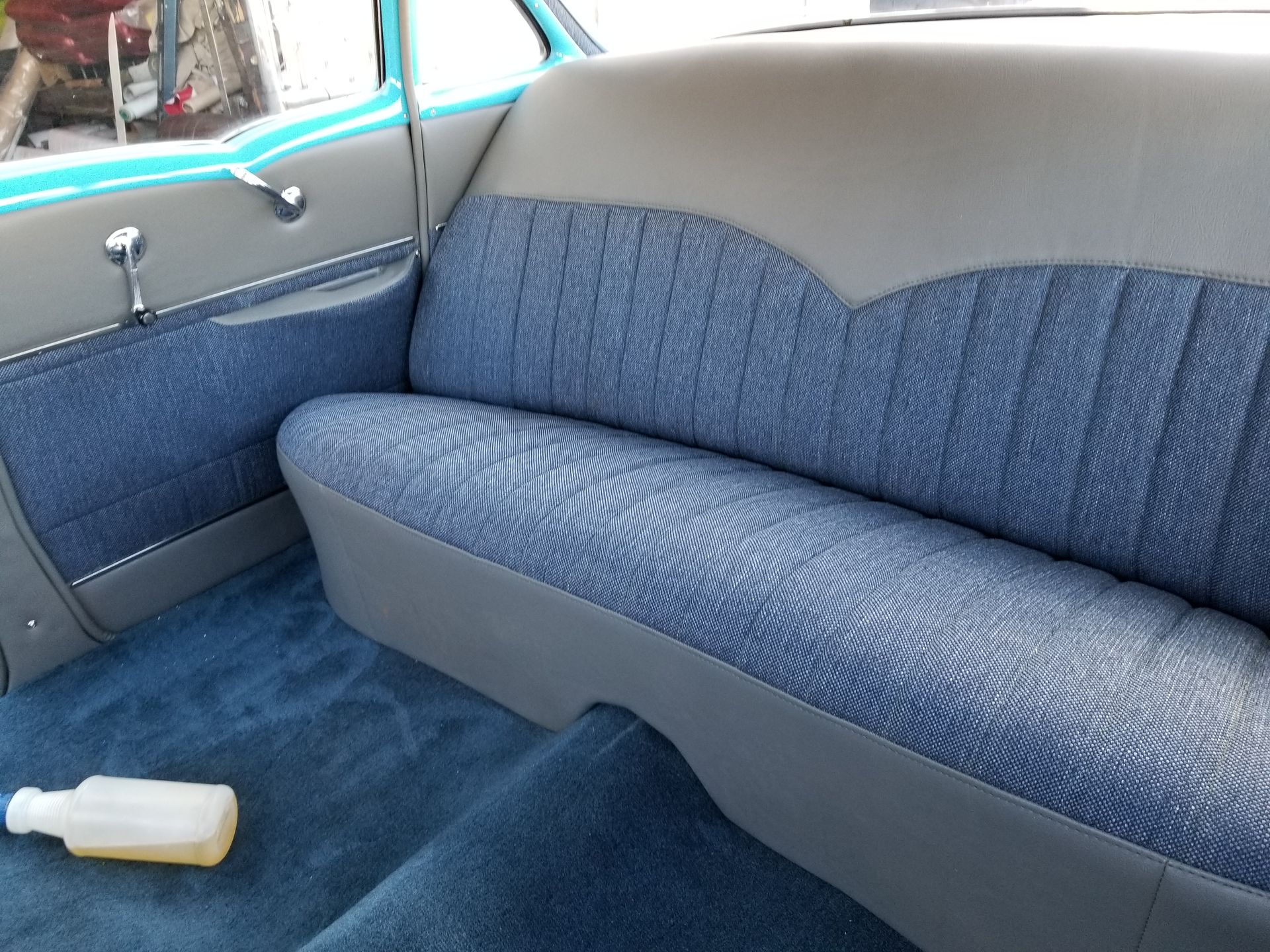 Blue and gray car backseat with patterned upholstery and a white bottle on the floor.