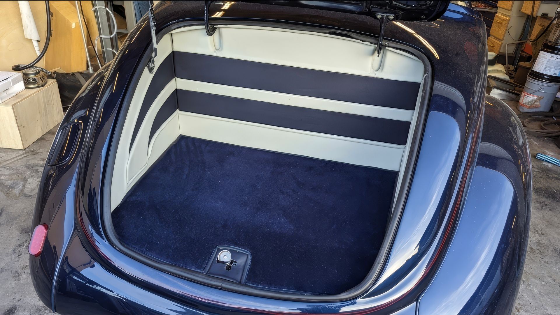Open car trunk with striped side panels and blue carpeted floor in a garage