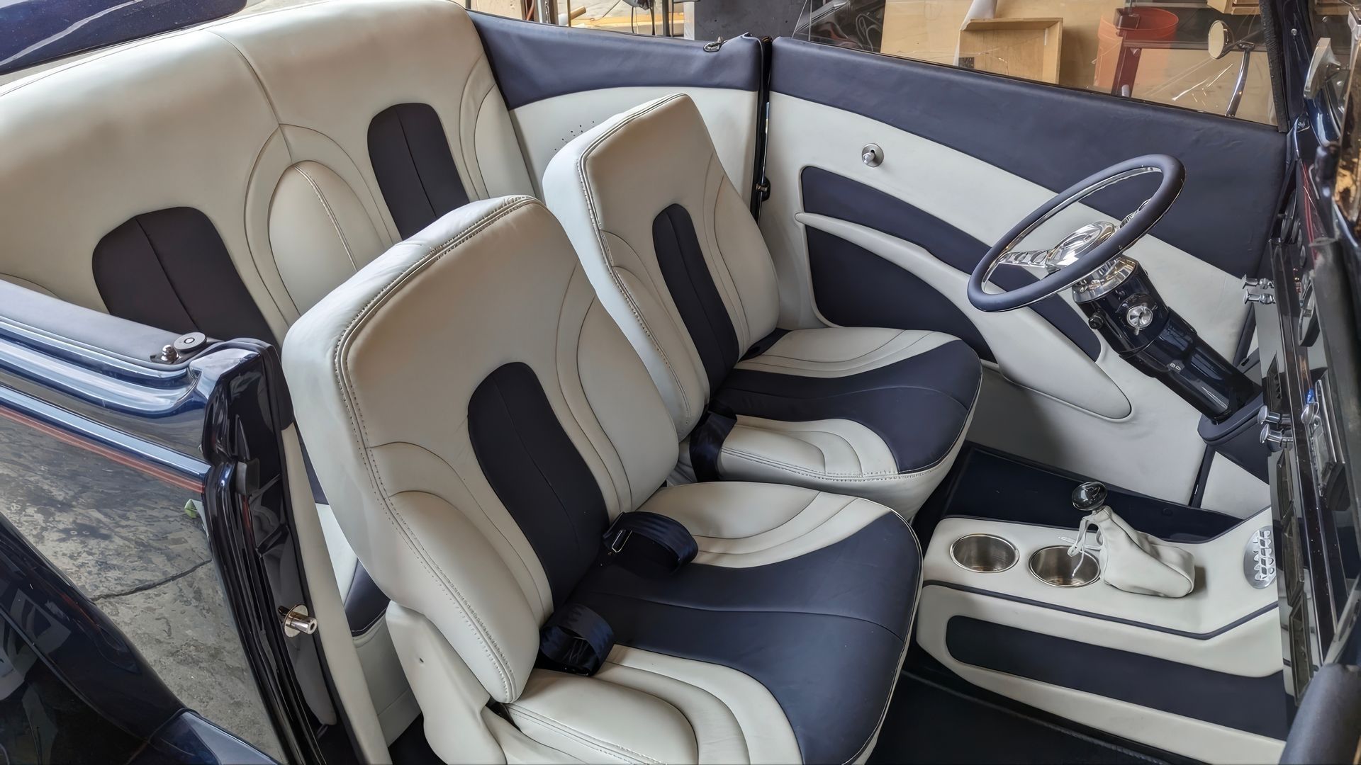 Cream and navy captain’s seats and helm in a boat cabin with a steering wheel and cup holders.