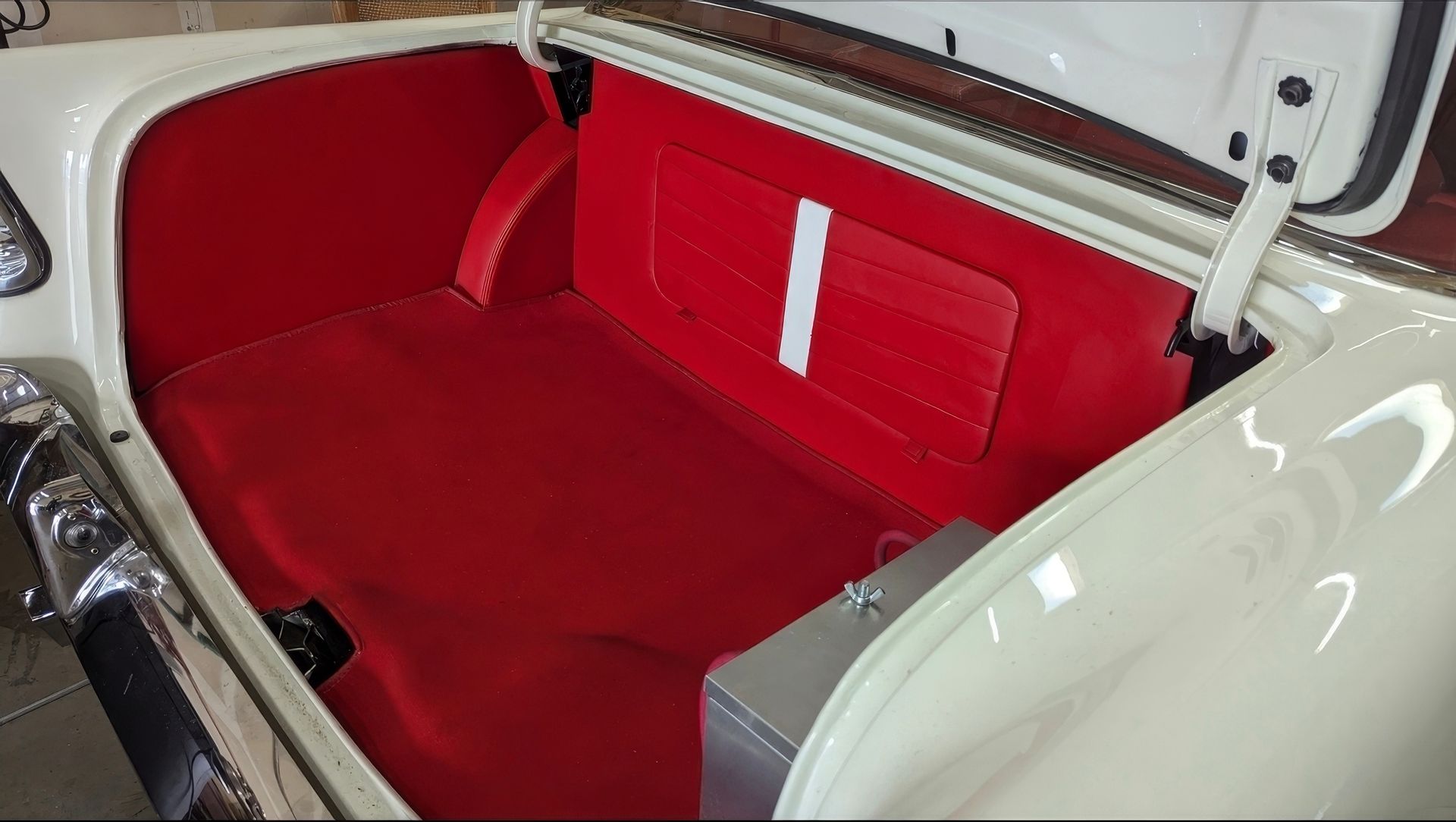 Red vintage car interior with a red leather bench seat and white exterior trim shown open from the rear.
