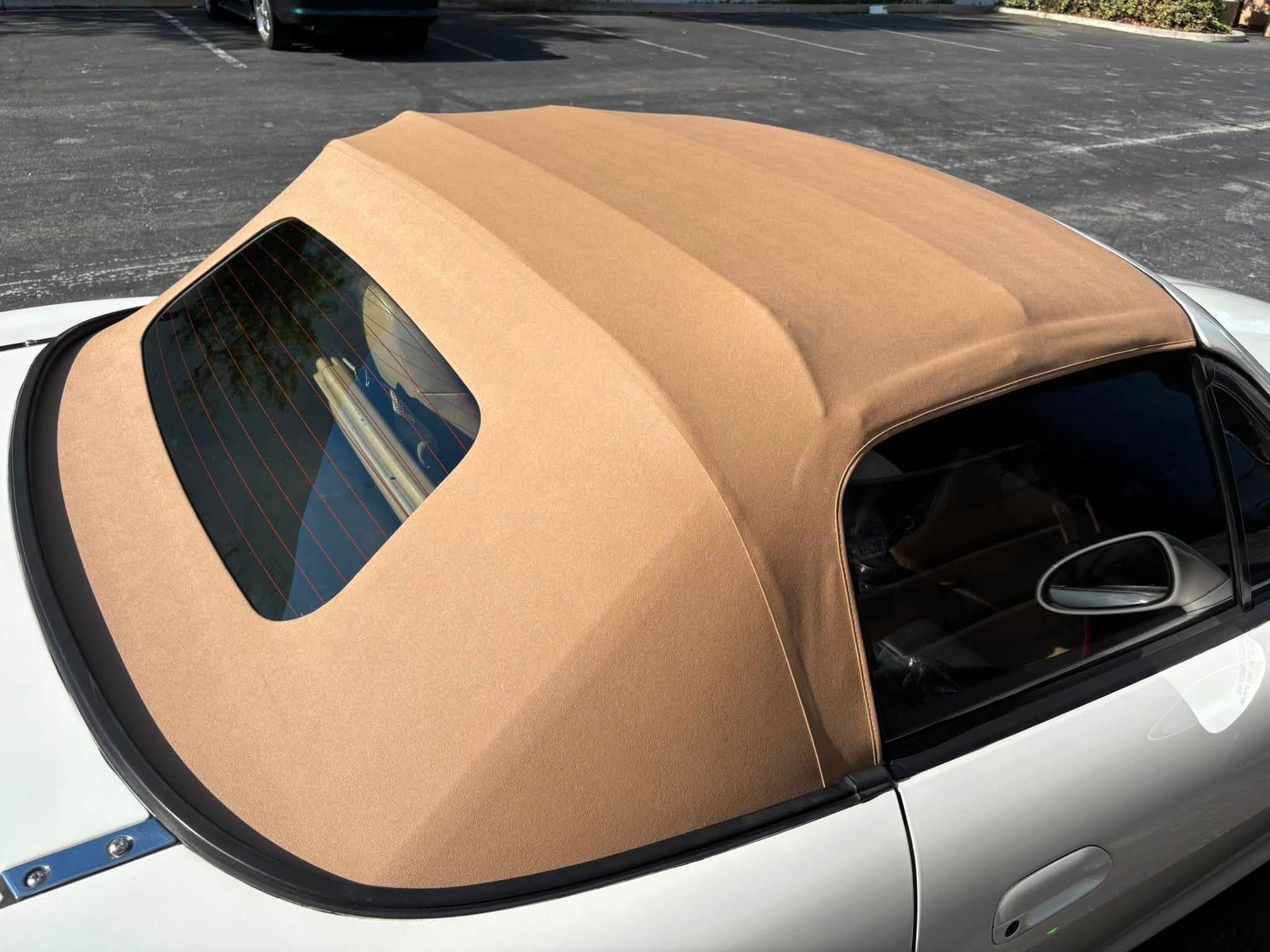 Car with a tan soft top convertible roof on a silver body, parked outdoors