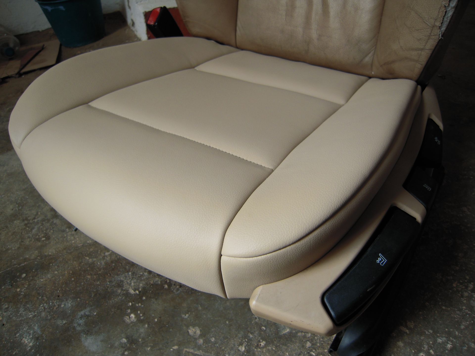 Beige leather car seat cushion with stitched center panels and black side controls on the right
