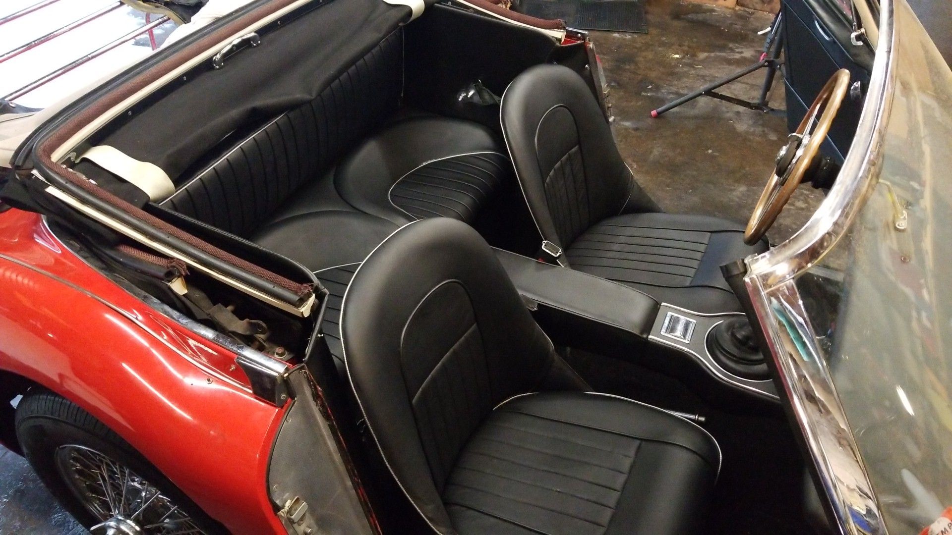 Red convertible interior with black leather seats and a chrome-trimmed windshield frame, viewed from above