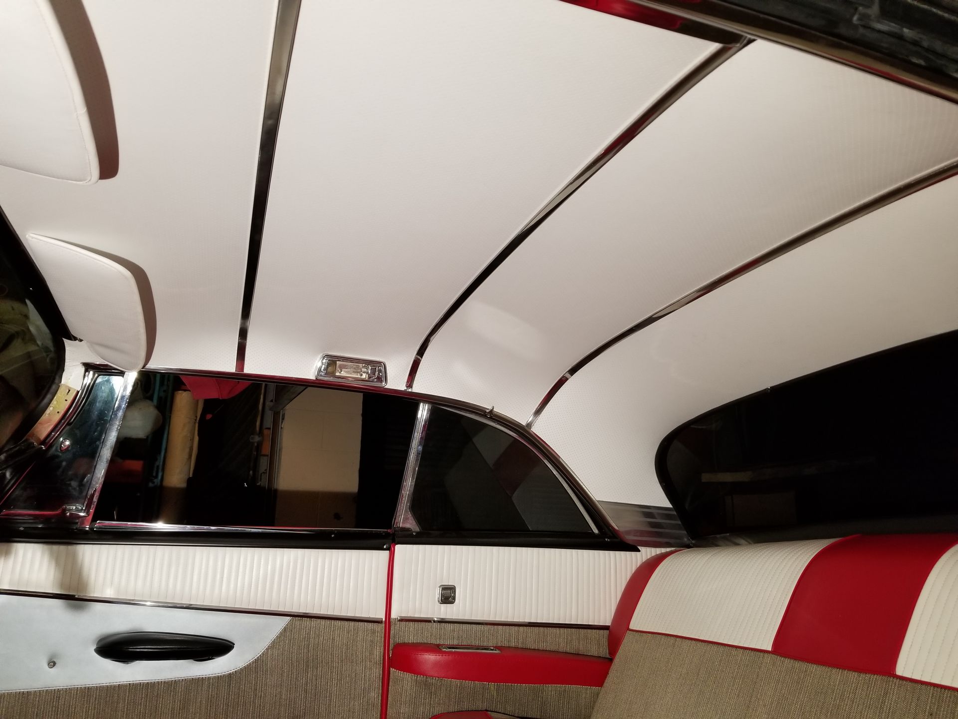 Inside a car interior with white, red, and black upholstery and curved ceiling panels.
