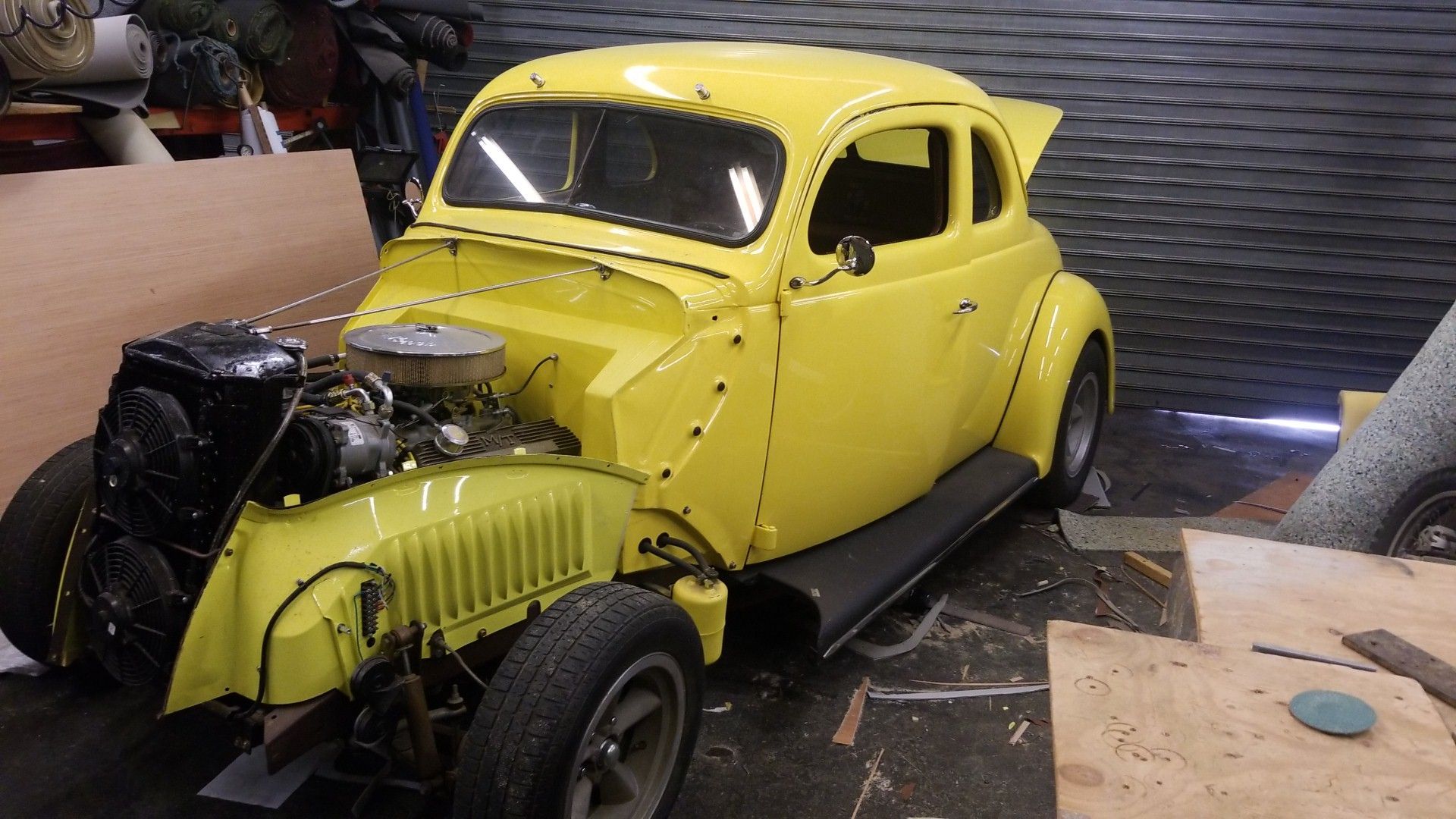 Yellow vintage hot rod car in a workshop, with exposed engine and black front end