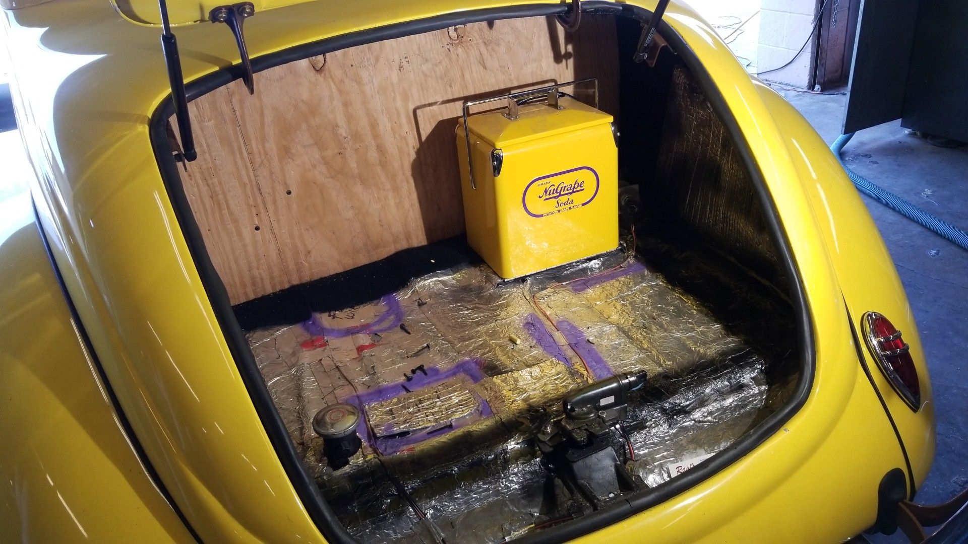 Yellow hatchback trunk lined with wood and foil, holding a yellow container inside.
