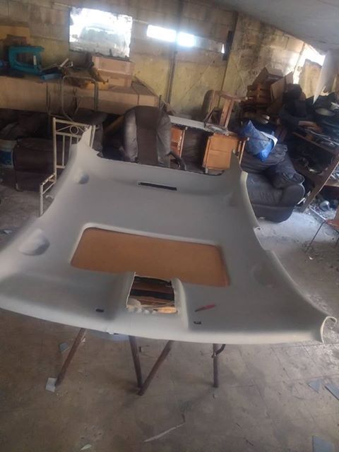 Car roof liner laid out in a dusty workshop, with tools and materials in the background.