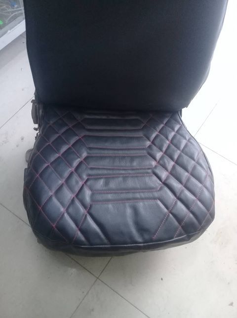 Black quilted seat cushion with red stitching on a chair, shown on a tiled floor