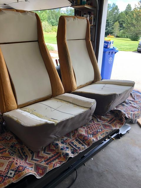 Two beige seat cushions on a vehicle bench with a patterned rug and open grassy background