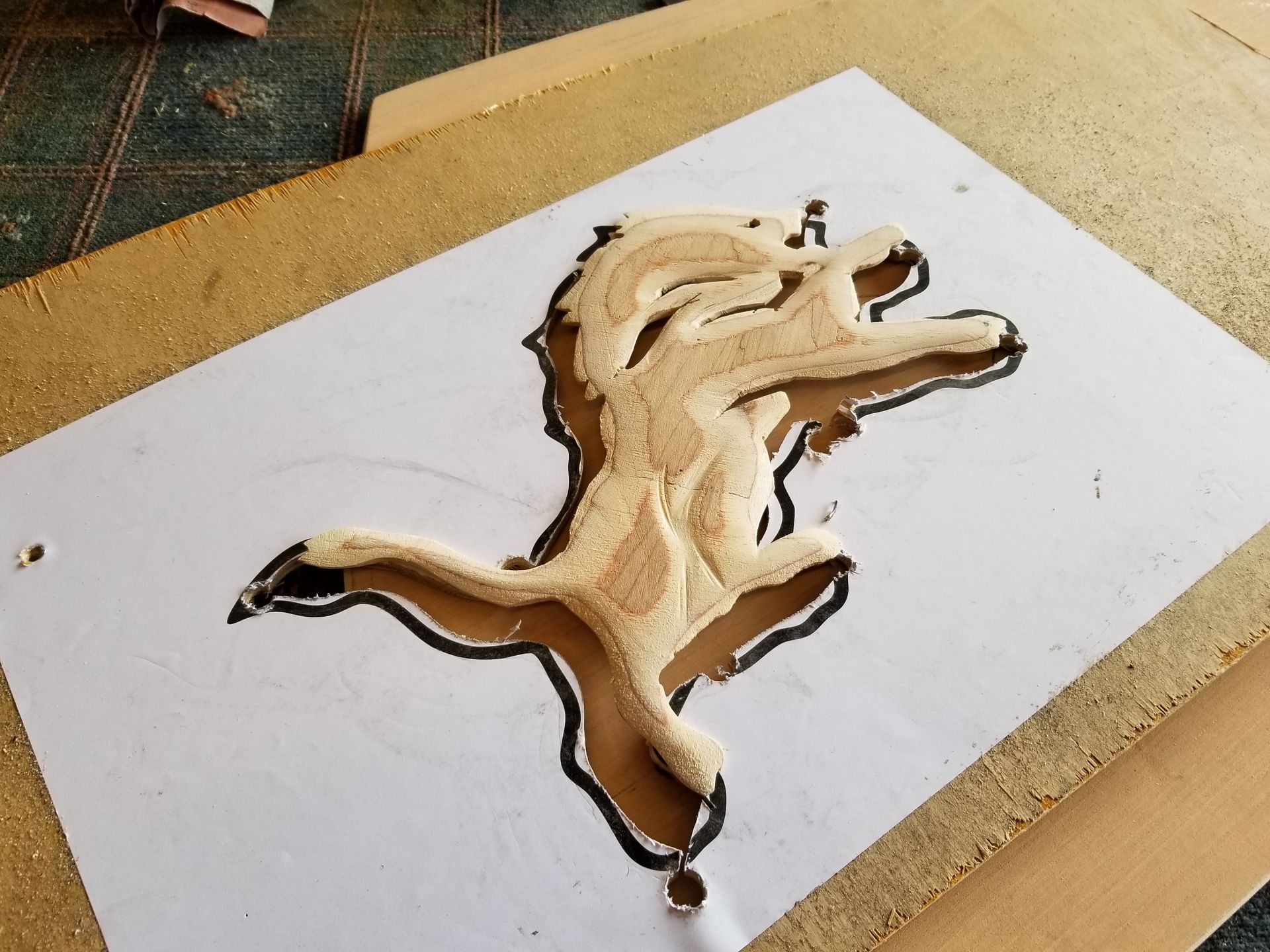 Carved wooden horse inlay on a white rectangular board with dark outline, lying on a work surface