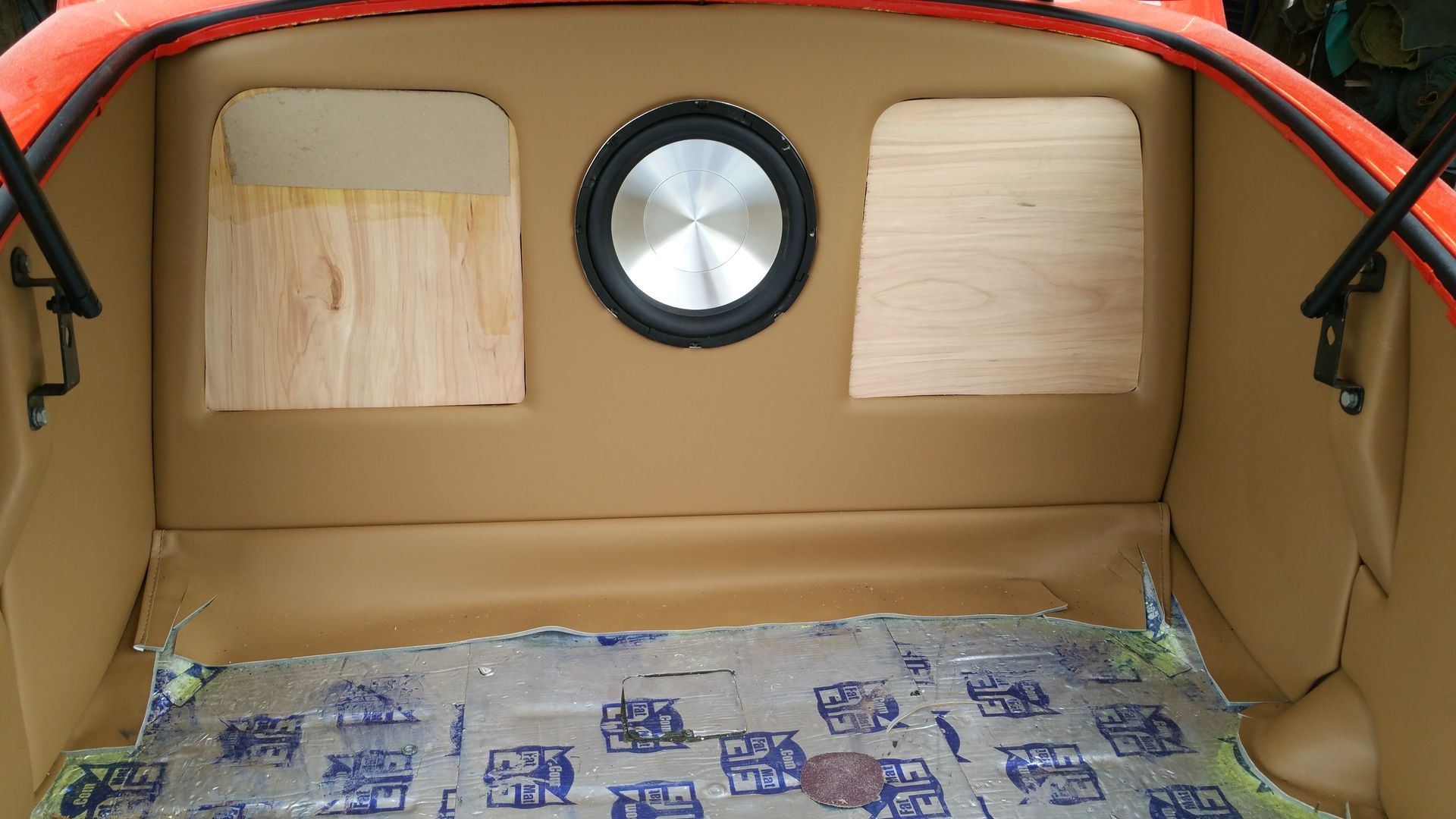 Interior of a small cardboard and wood play vehicle with a round window and patterned floor mat.