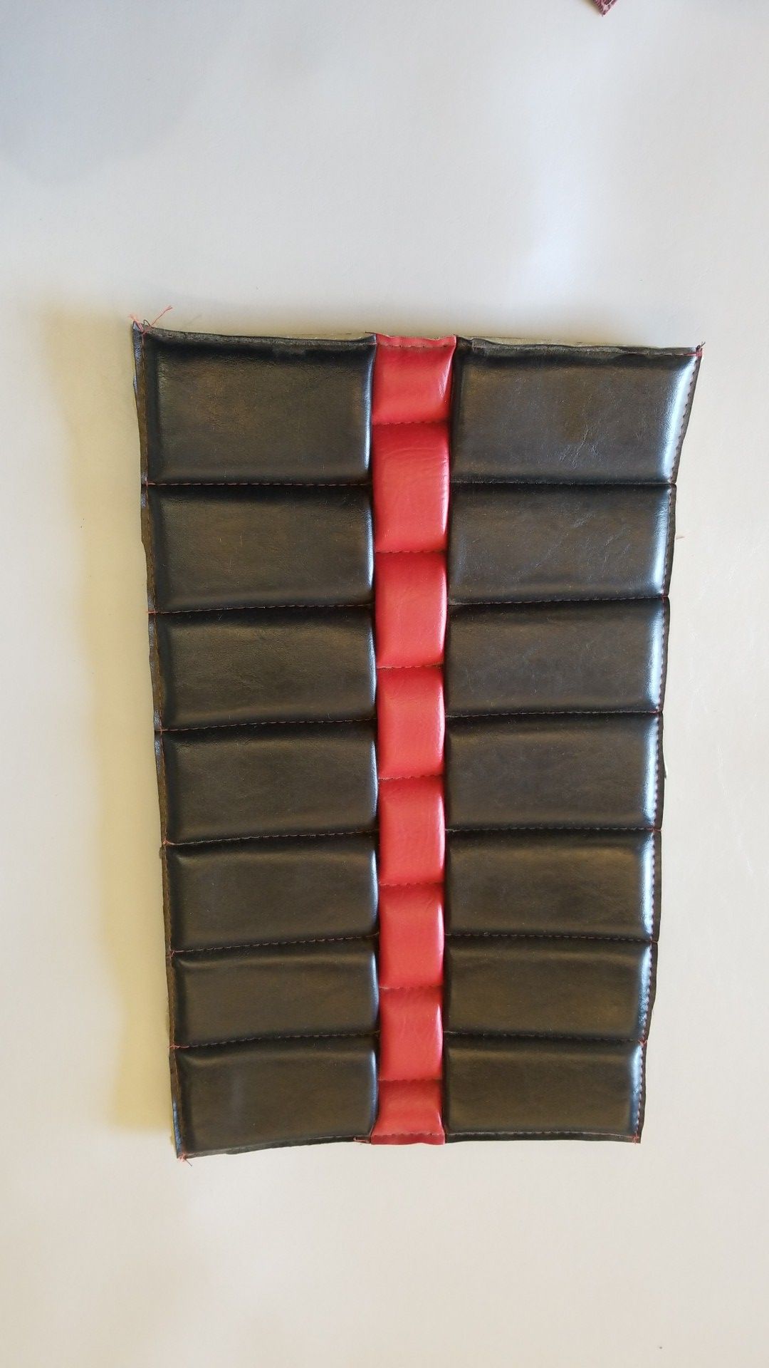 Black rectangular pouch with horizontal stitched sections and a red vertical center strap on a white background