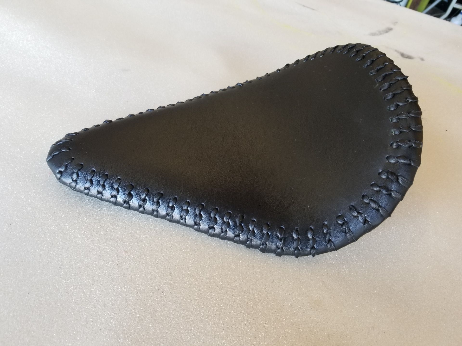 Black leather bicycle saddle with stitched edges on a light surface