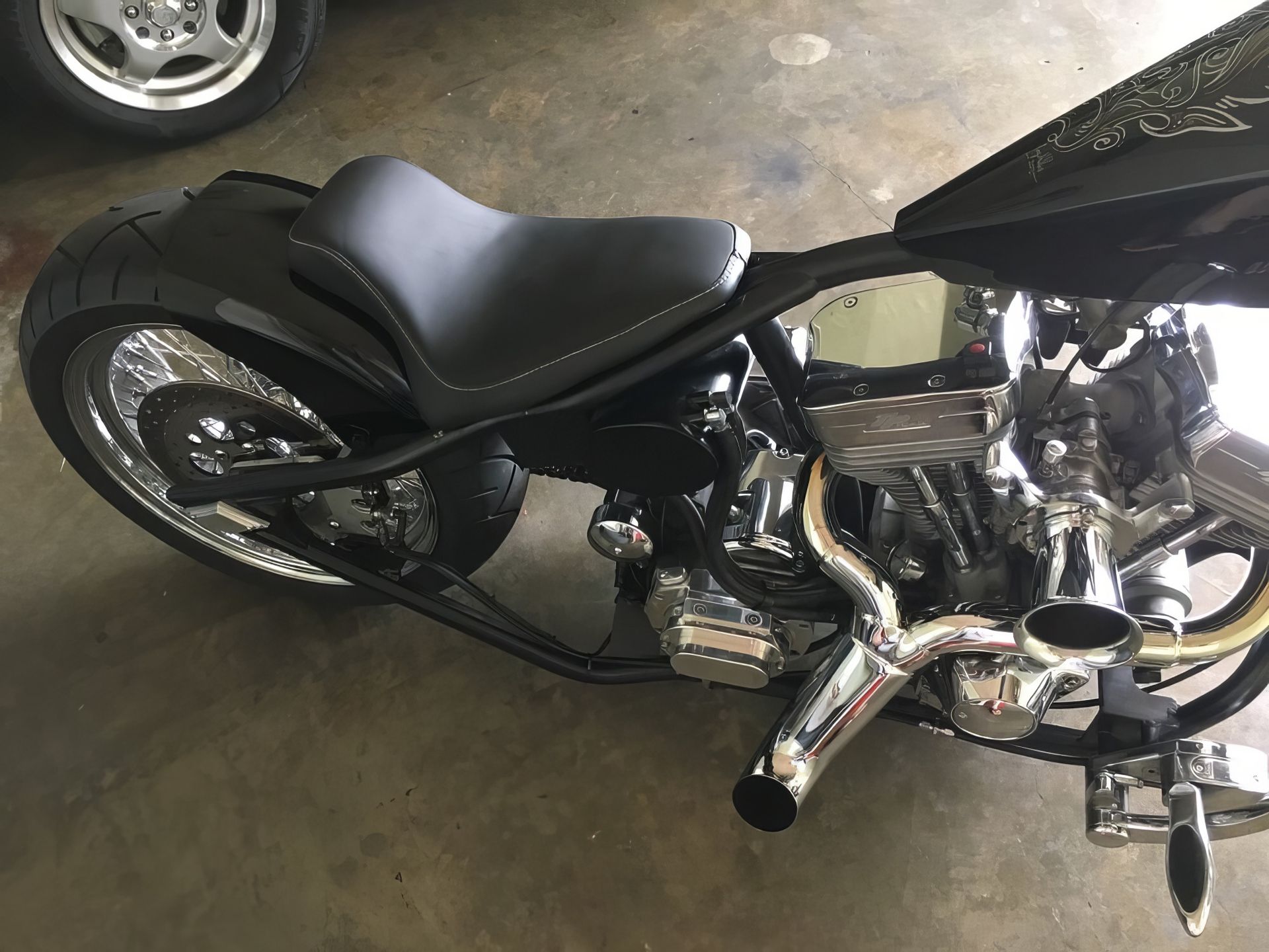 Black custom motorcycle parked in a garage, side view with chrome engine and exhaust visible