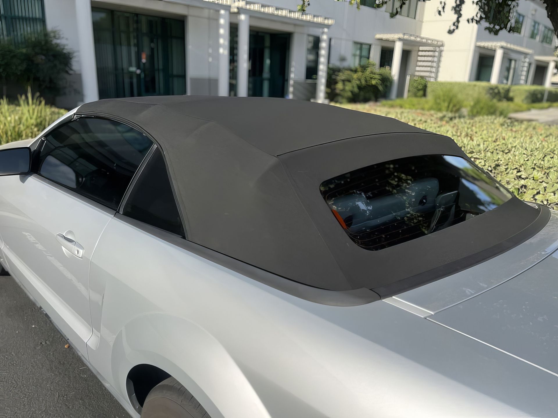 Gray convertible with black soft top parked in front of a house and landscaping