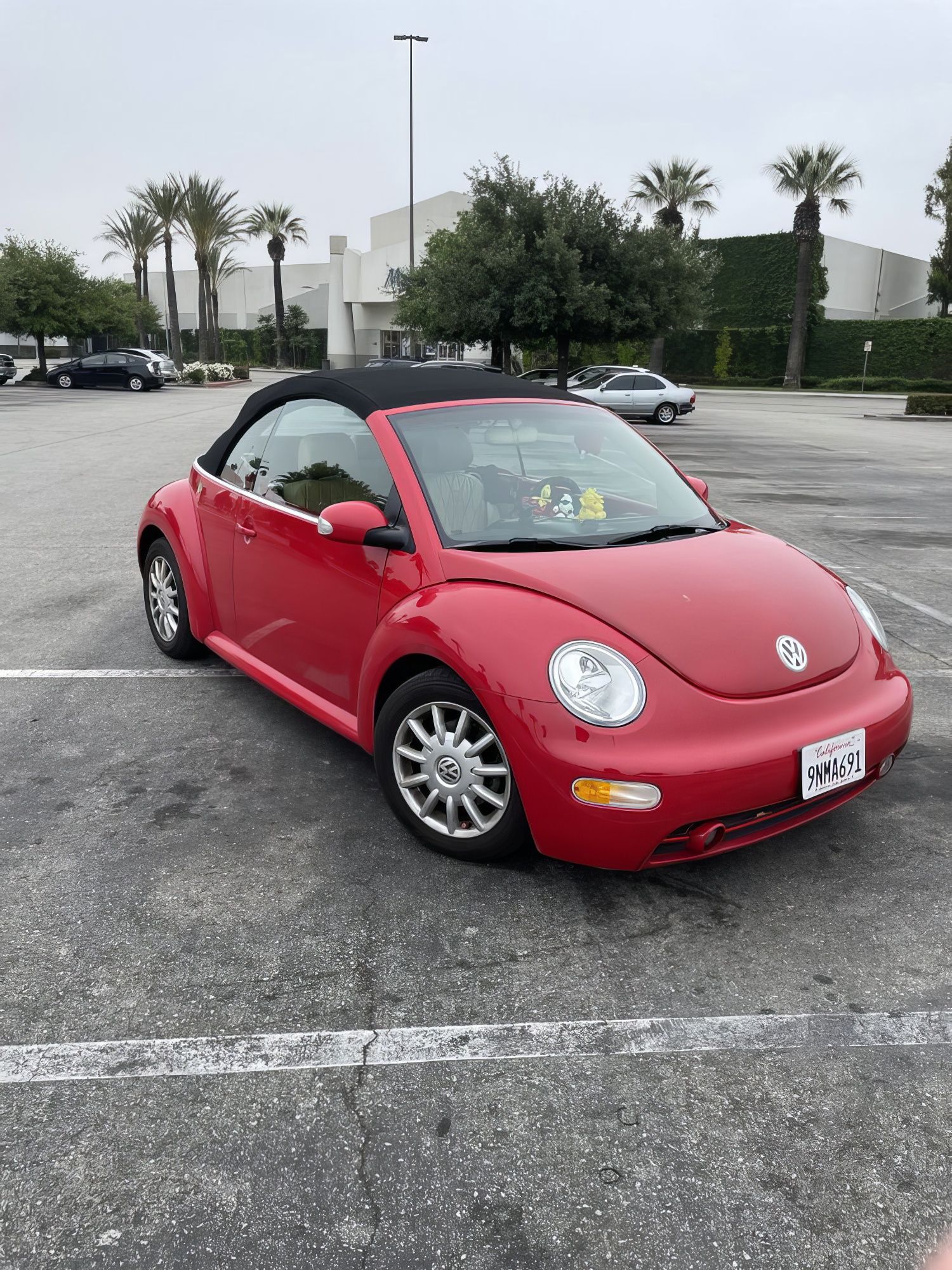 Red Volkswagen Beetle convertible parked in a wet lot under an overcast sky.