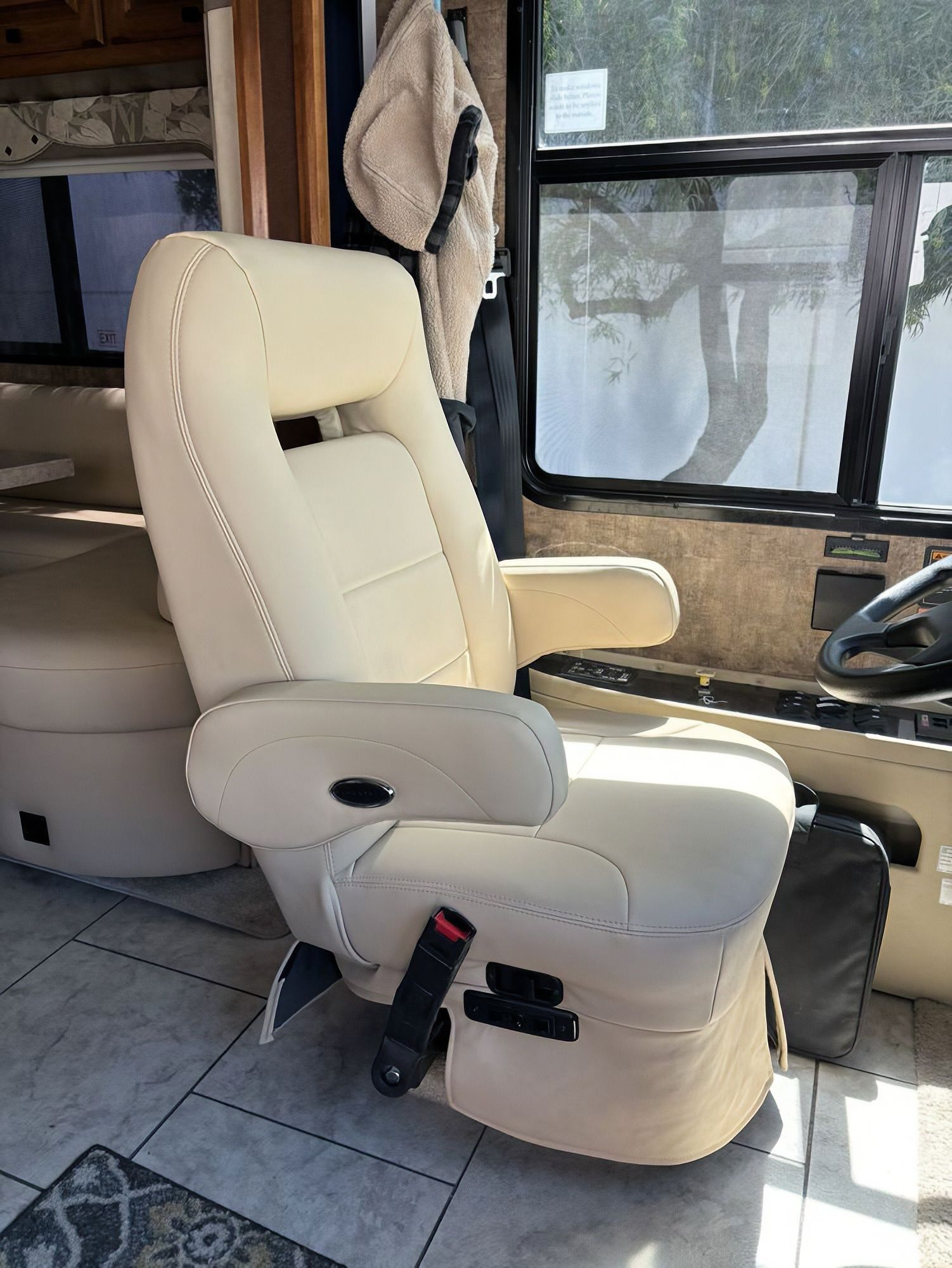 Cream leather reclining seat with armrests in a vehicle interior near a steering wheel and window.