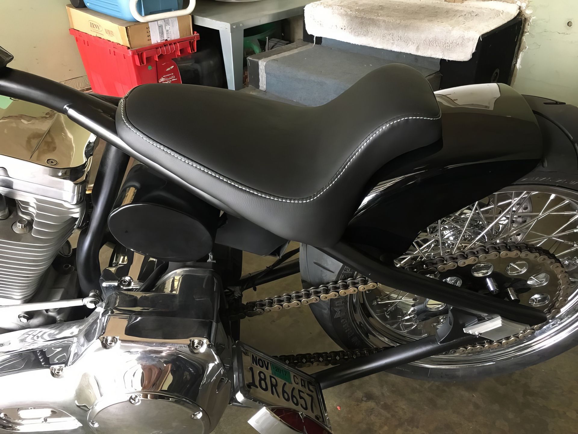 Black motorcycle seat and chrome engine in a garage, with rear wheel and chain visible.