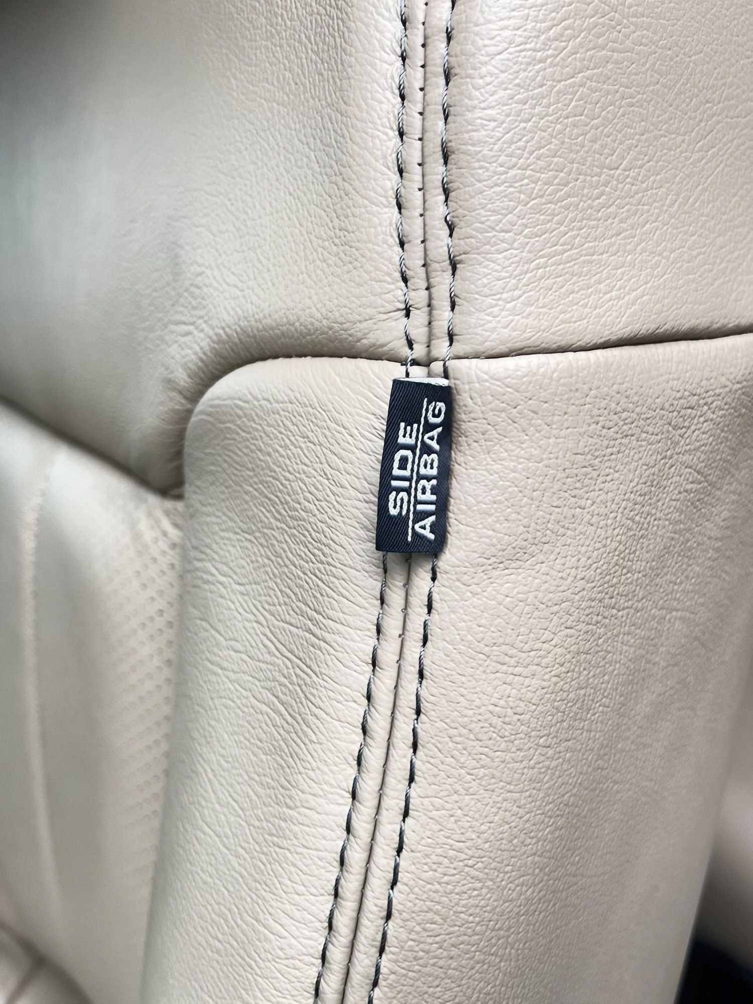 Close-up of a light gray leather seam with a black ALIEN WORKS tag.