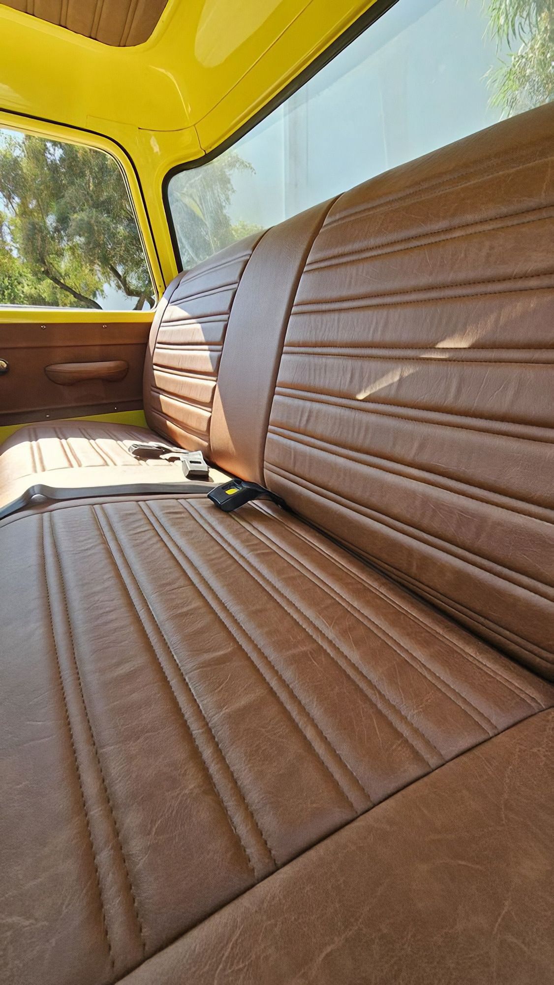 Tan and brown vinyl car seat interior with yellow roof and window view of greenery